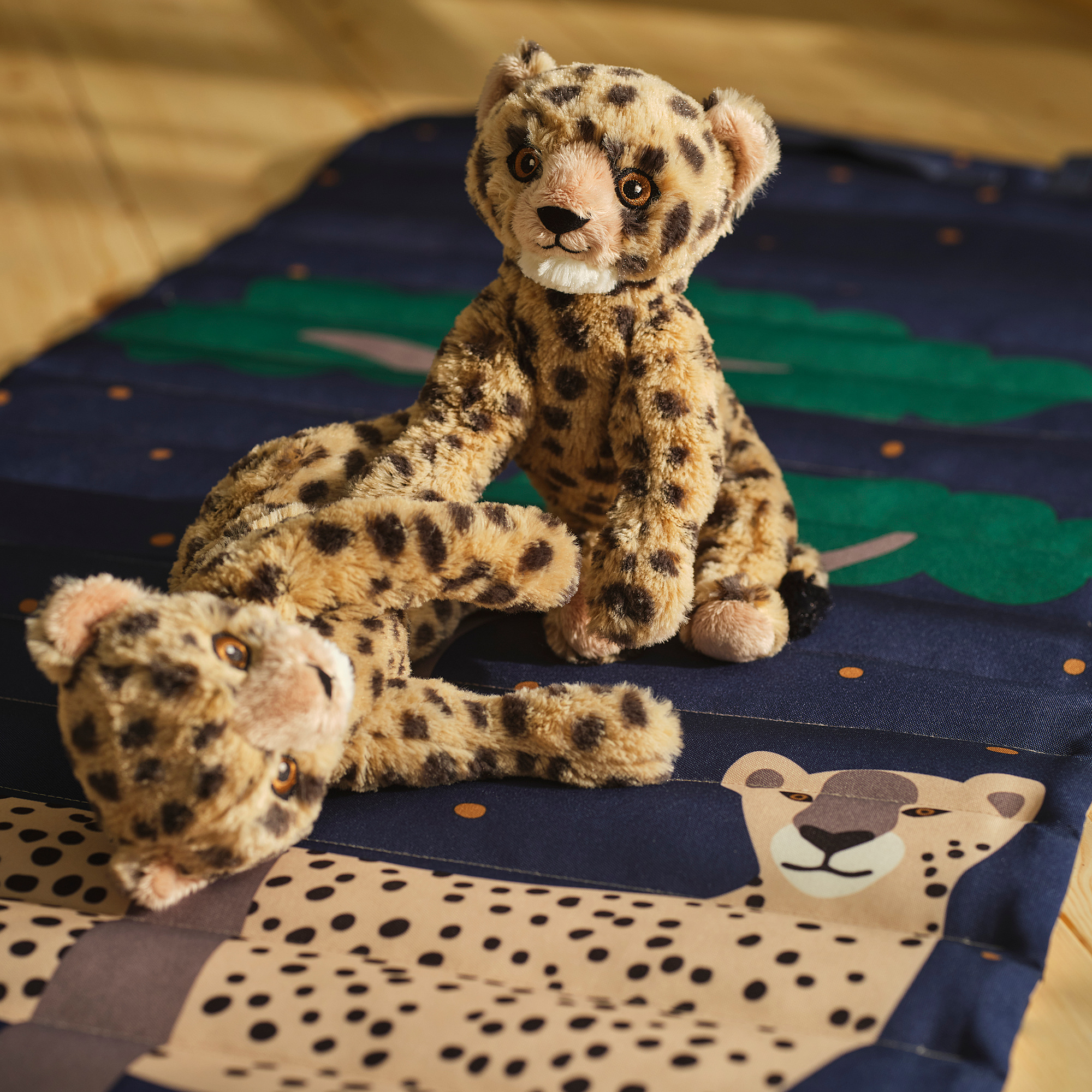 Two cheetah plush toys on striped blanket; one standing, one lying. Realistic textures, approx. 10 inches each.