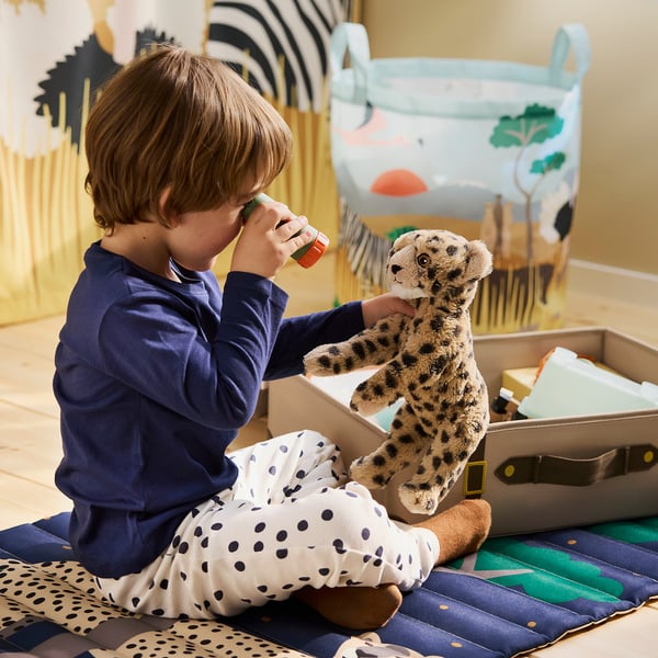 Child plays with toy cheetah. Holds toy to ear, listening. Box and mat with toys nearby.