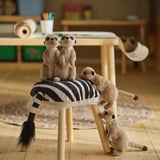 Meerkat stuffed animals on a stool; two sitting, one standing, one lying. Childs room with wooden floor and table.