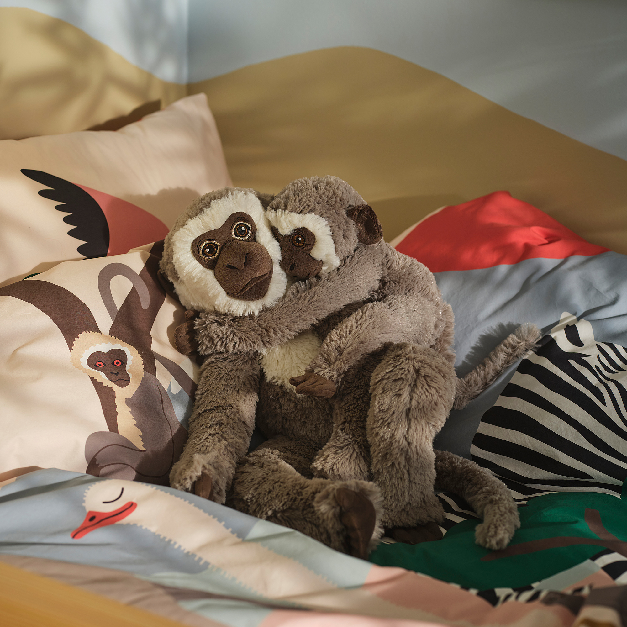 SANDLÖPARE: cozy grey stuffed monkeys on colorful bedding, large and plush.