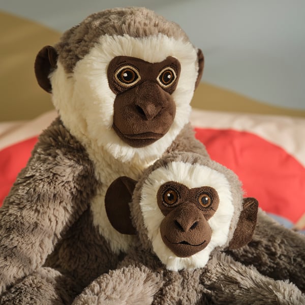 Two plush monkeys, one large, one small, both brown and white, sitting together. The larger monkey holds the smaller one.