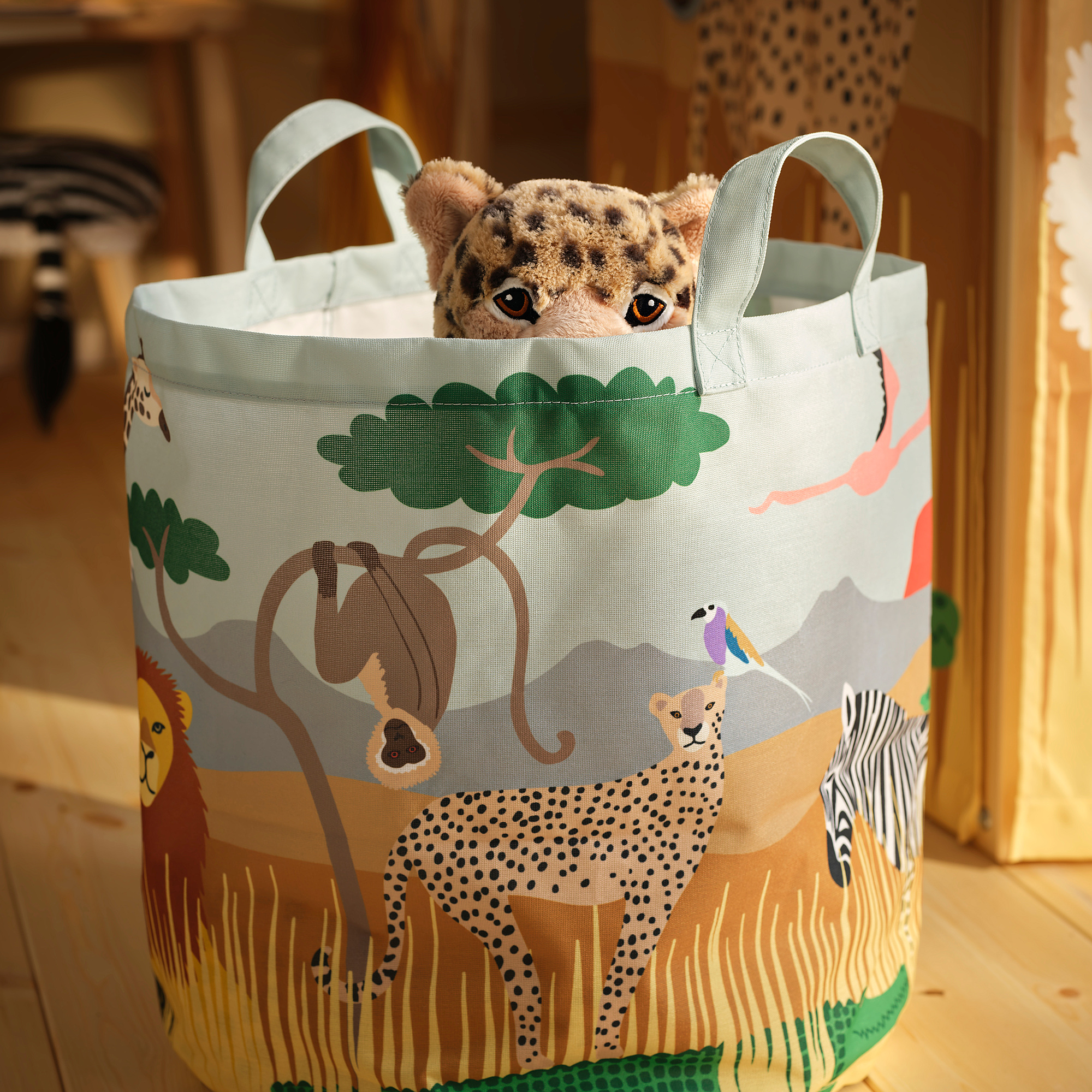 Stuffed cheetah peeking from large, colorful, savannah-themed storage bag with sturdy handles.