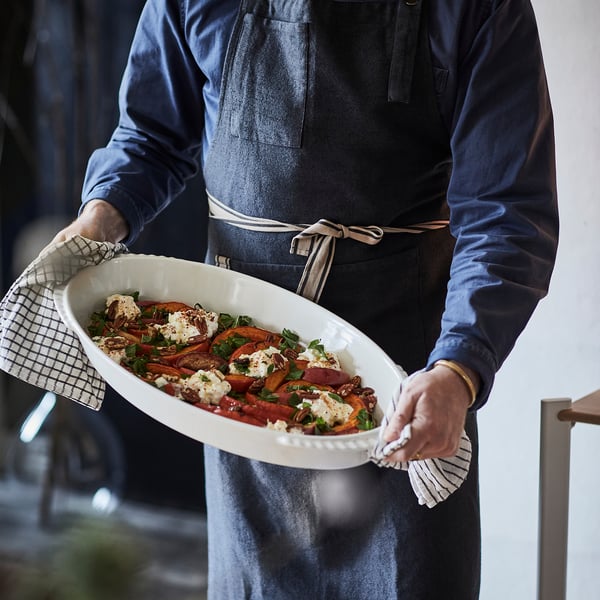 Person wearing a SANDVIVA apron, holding a dish with food, showcasing the aprons protective function and practical pockets.