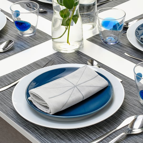 Well-set dinner table with blue plates, white napkins, silverware, and clear glasses. Centerpiece has small green plant.