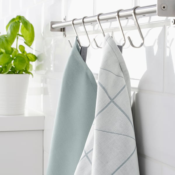 Two light blue towels hang on silver hooks under a white shelf. A green plant sits on the left.