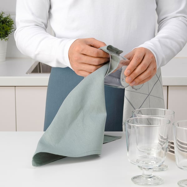 Person folding light blue cloth on white table with empty glasses.