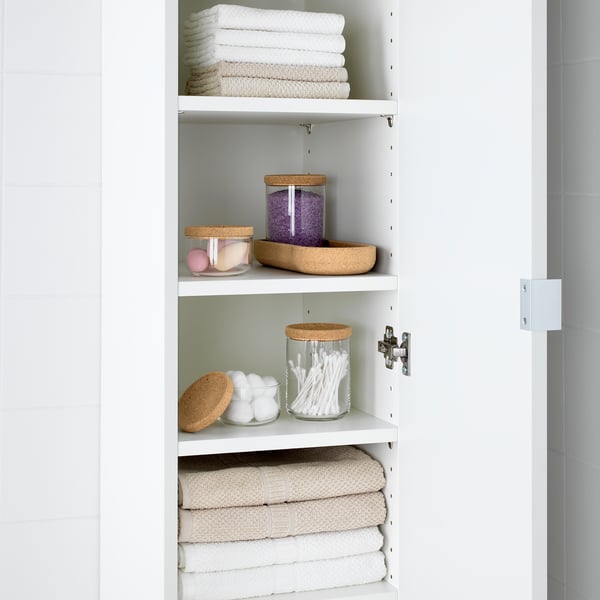 White shelving unit with stacked towels and storage jars. Jars hold cotton swabs, bath bombs, and small items.