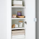 White shelving unit with stacked towels and storage jars. Jars hold cotton swabs, bath bombs, and small items.