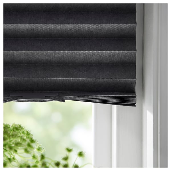 A dark grey SCHOTTIS roller blind, partially drawn on a white window, featuring recycled polyester and blocking light.