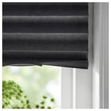 A dark grey SCHOTTIS roller blind, partially drawn on a white window, featuring recycled polyester and blocking light.