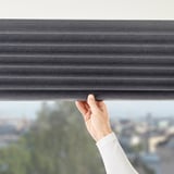 Person adjusts grey block-out blind, controlling light in room.