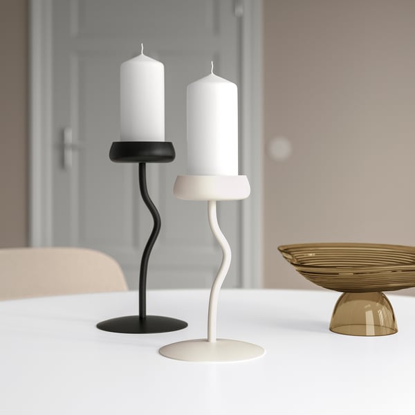 Black & white candlesticks with tall candles; black one shorter, white one taller. Scandinavian design. Golden bowl in background.