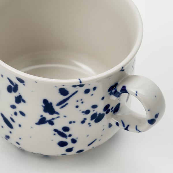 Close-up of white mug with blue splatters, smooth glaze, sturdy handle.