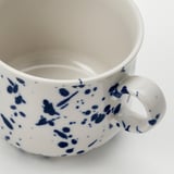 Close-up of white mug with blue splatters, smooth glaze, sturdy handle.