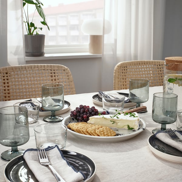 Table set with SILVERSIDA glassware, plates, and cutlery. Includes a cheese platter, crackers, and grapes. Wicker chairs surround the table.