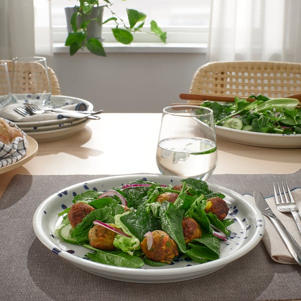 Salad, falafel, and water on table. Another salad and plates in background.