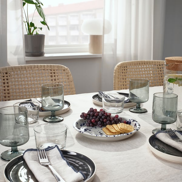 Table set with SILVERSIDA glassware and plates. Plates hold grapes and crackers. Wicker chairs surround the table.