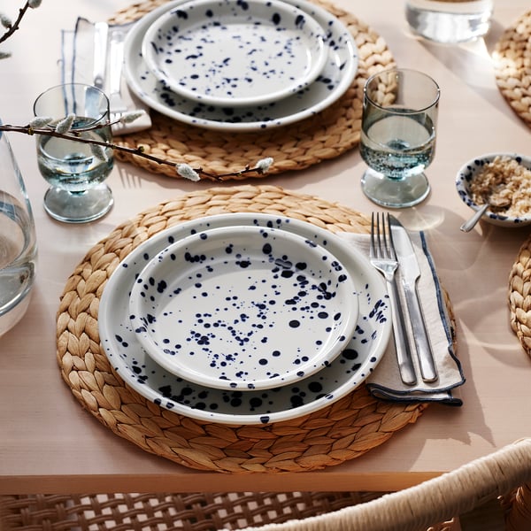 Rustic table setting with white-blue dotted plates, woven placemats, glassware, and cutlery.