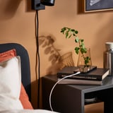 Bedside scene with books, plant, and charging cable.