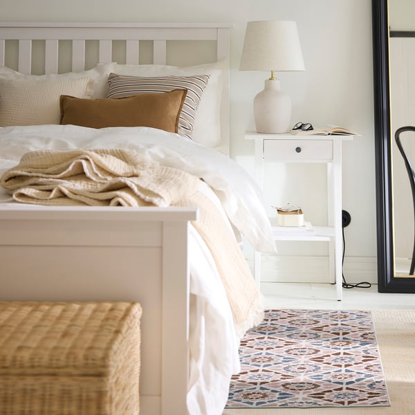 Cosy bedroom with white bed, brown pillows, bedside table, lamp, and a SJÖINGENJÖR rug.