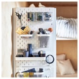 White SKÅDIS pegboard storage system with various accessories like baskets, bins, and containers holding beauty and office supplies.