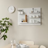 Wall-mounted pegboard SKÅDIS with shelves and kitchen tools; clock and plant nearby.