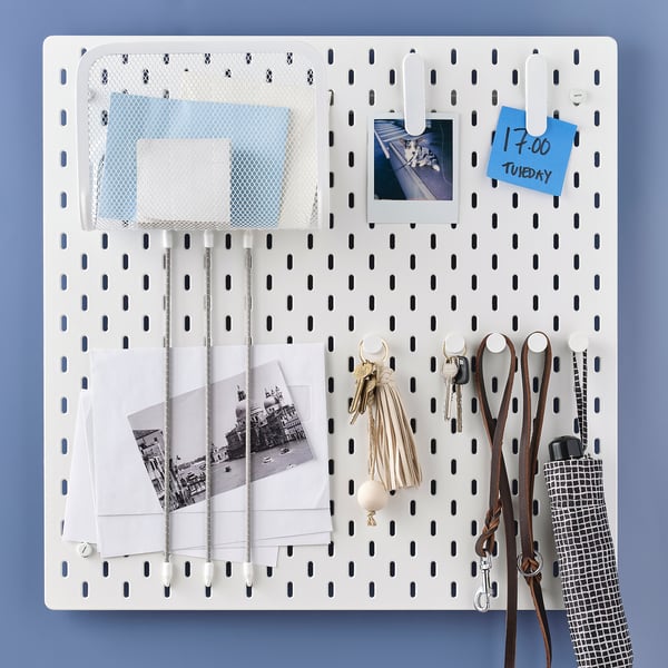 White SKÅDIS pegboard with accessories: mesh basket, notes, photos, keys, purse, and umbrella hooks. Ideal for organizing and displaying items.