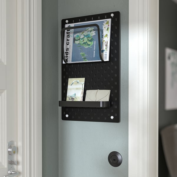Black SKÅDIS pegboard on door, displaying items in pockets and shelf.