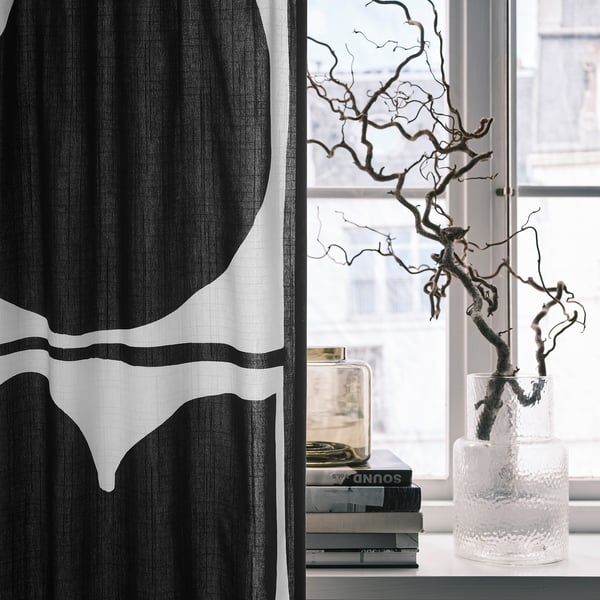 Black & white leaf curtain beside window with vase and books.