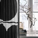 Black & white leaf curtain beside window with vase and books.