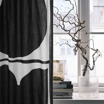 Black & white leaf curtain beside window with vase and books.