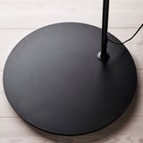 Black round floor lamp base with smooth finish and circular design on wooden floor.