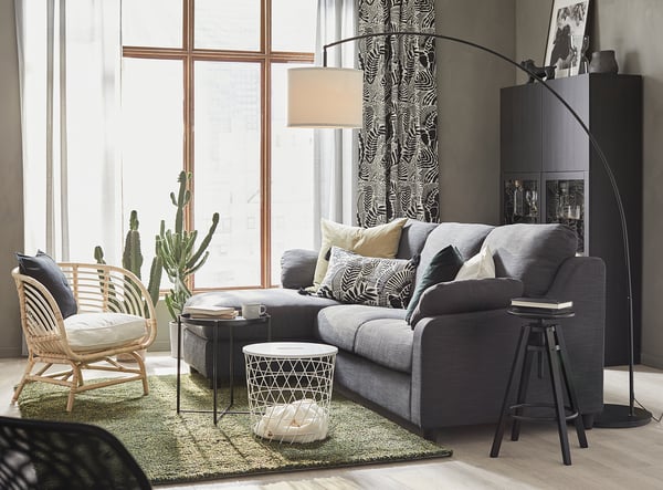 Modern living room with gray SKAFTET floor lamp, sofa, wicker chair, cacti, and black cabinet.