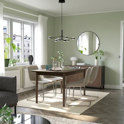 Green dining room with brown table, grey chairs, plants, and windows. Seats 4-6.