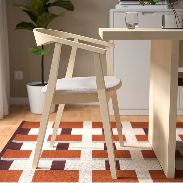 A light wooden table with a leaf extension sits on a geometric rug, paired with comfortable cushioned chairs, ideal for dining or workspaces.