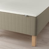 Close-up of SKÅRER sprung mattress on wooden legs from ikea. Mattress pad visible, with light-colored fabric.