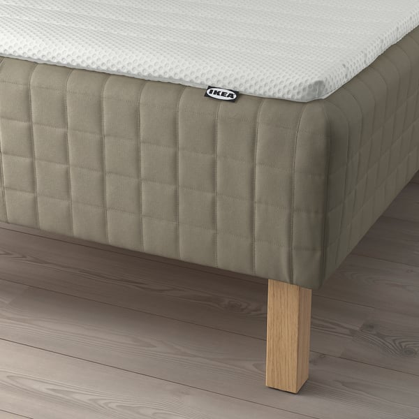 IKEA SKÅRER mattress pad on wooden base over light wood floor. Small IKEA tag visible.