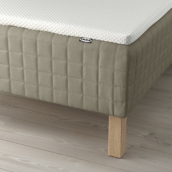 A bed with a green fabric base, wooden legs, and a white mattress, providing supportive pocket springs and a comfortable foam mattress pad.
