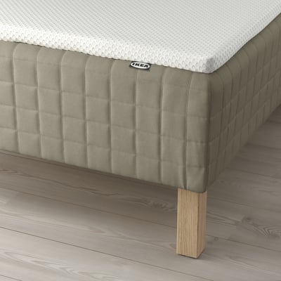 A bed with a green fabric base, wooden legs, and a white mattress, providing supportive pocket springs and a comfortable foam mattress pad.