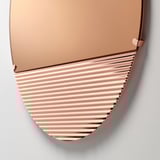 SKOGSGRÄNSEN mirror, rose-gold toned, wavy bottom reflection, mounted on white wall.