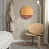 Modern bedroom with large rose-gold SKOGSGRÄNSEN mirror, above wooden chair, reflecting stylish, natural horizon design.