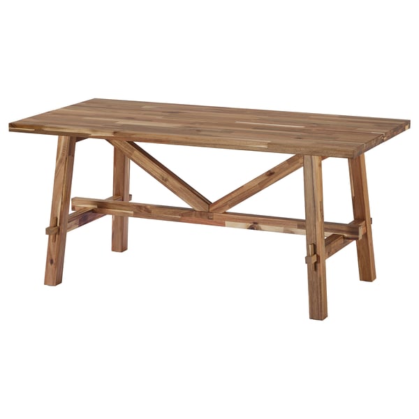 A light brown SKOGSTA acacia wood dining table with a rectangular top and trestle-style legs.