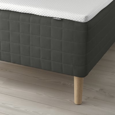 Dark quilted bed base with light wooden legs supporting a white mattress.