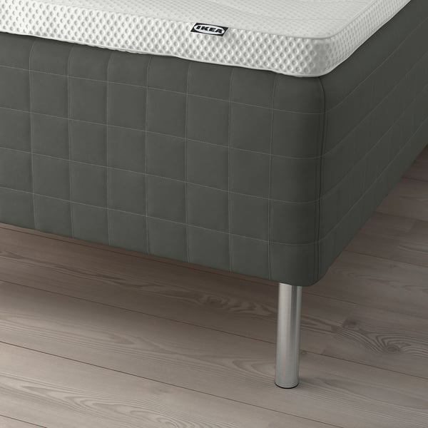 Close-up of SKOTTERUD mattress with detailed white topper on dark base, supported by metal legs on wooden floor.