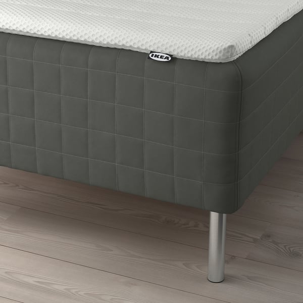 A bed with a dark green SKOTTERUD mattress on wooden legs. The brown wooden floor is visible.