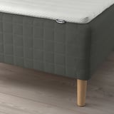 A bed with a dark gray SKOTTERUD mattress on wooden legs, showing the IKEA tag.
