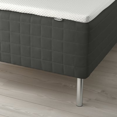 Close-up of a dark grey ikea mattress with visible spring technology and sleek metal legs on a wooden floor.
