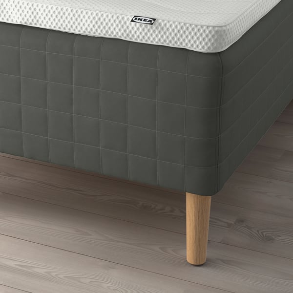 Close-up of corner of SKOTTERUD mattress on IKEA bed frame with wooden legs and padded underside.