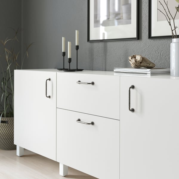 White cabinet with antique handles, displaying decorative items, including candlesticks and books.