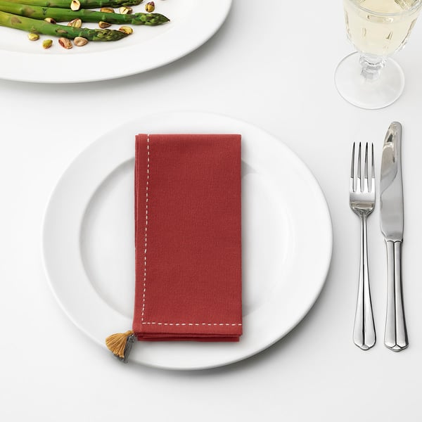 SLÄTTIKA red napkin, small with tassel, on plate, knife, fork, glass, asparagus nearby.